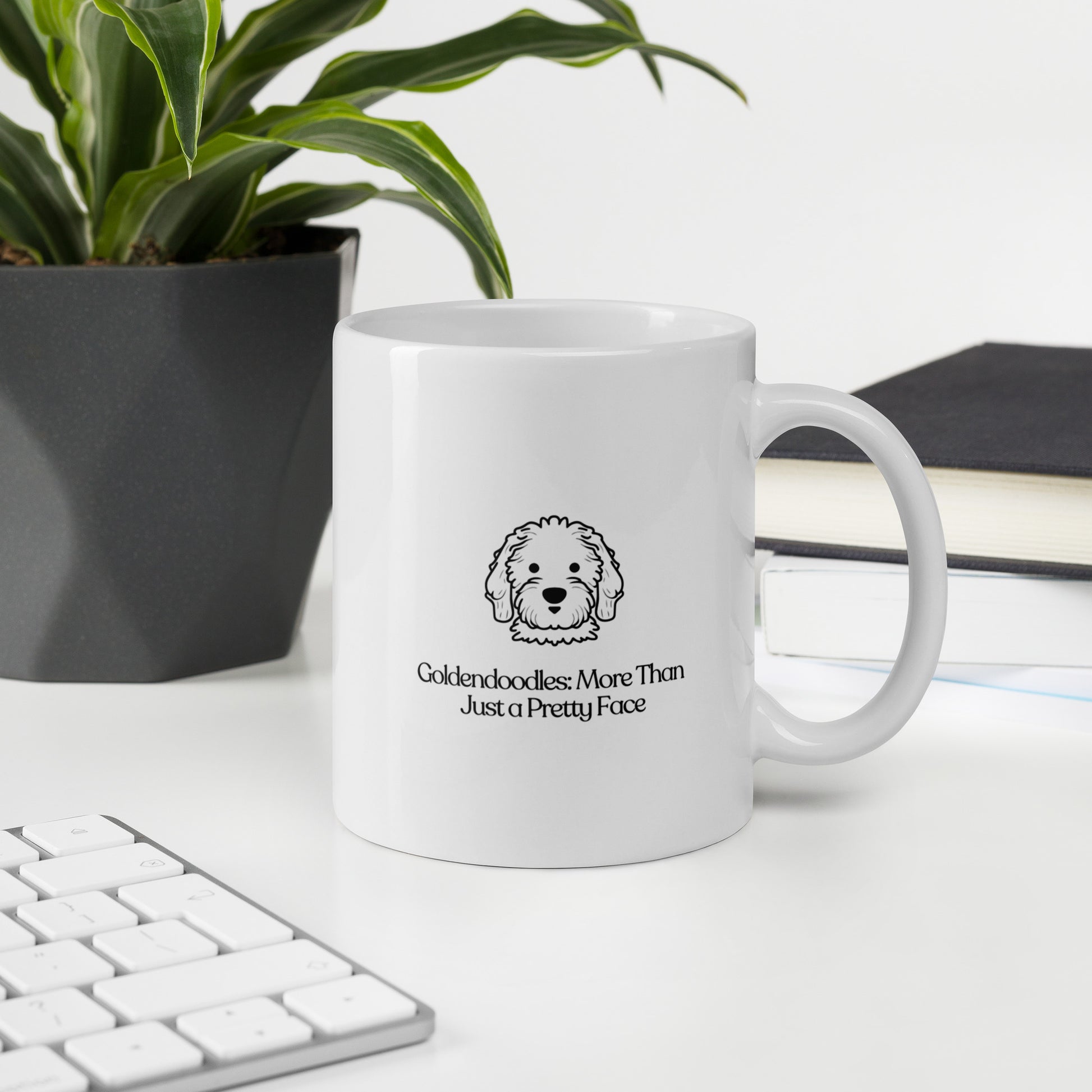 white color glossy ceramic mug that says goldendoodle more than just a pretty face on a desk with a book, keyboard and plant in the background